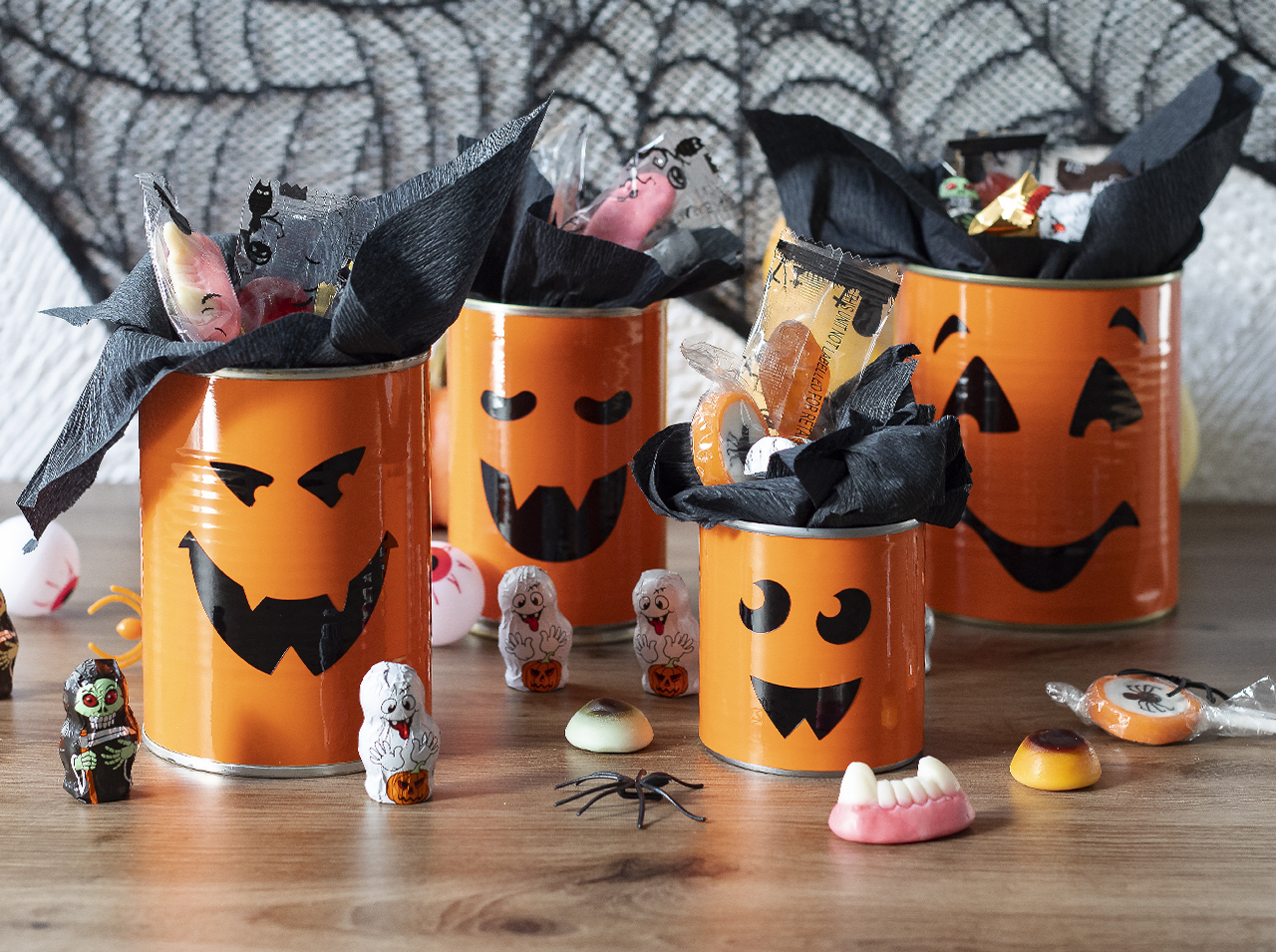 Upcycling DIY: Tin cans with d-c-fix® adhesive foils orange and black in the look of Halloween pumpkins with faces.