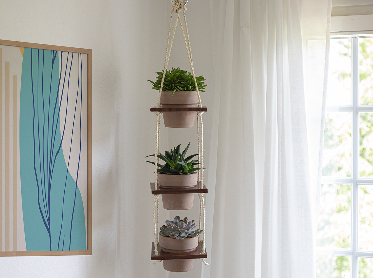 A shelf hanging from the ceiling made of three square wooden panels covered with wood-effect foil in walnut look, attached to four cords, and which the plant pots are inserted into.