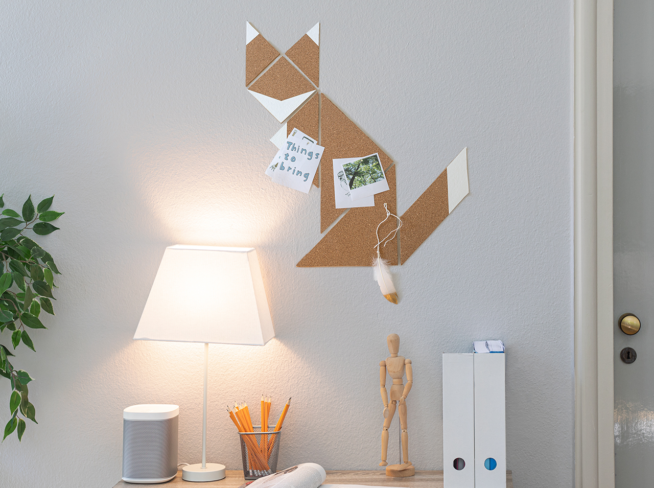 Modern cork pinboard in the shape of a fox with geometric decoration in white hanging on a wall by the desk.